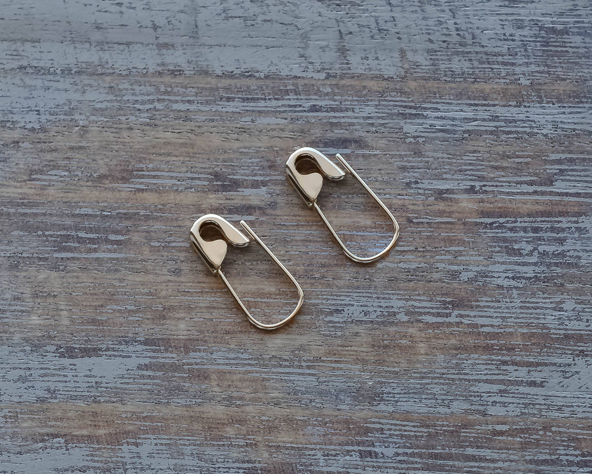 Silver mini safety pin earrings with a sleek, edgy design on a rustic wooden surface.