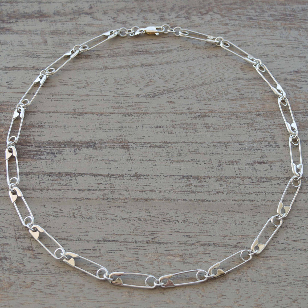 Sterling silver chain necklace with elongated oval links and a secure lobster clasp closure on a wooden surface .