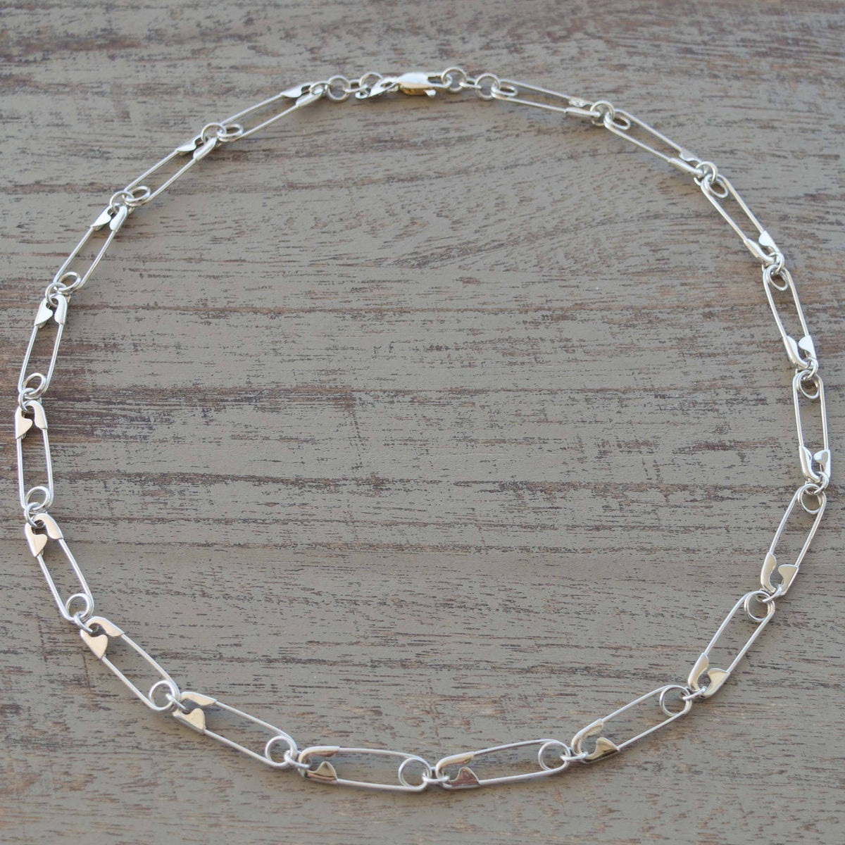 Sterling silver chain necklace with elongated oval links and a secure lobster clasp closure on a wooden surface .