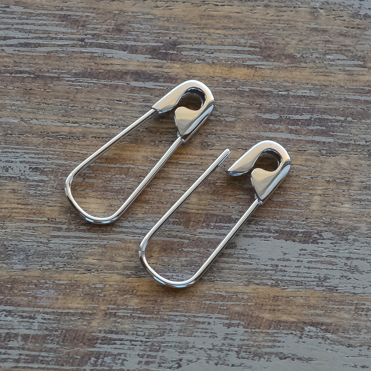 Sterling silver hoop earrings shaped like 3/4" safety pins with a polished finish on a wooden surface.