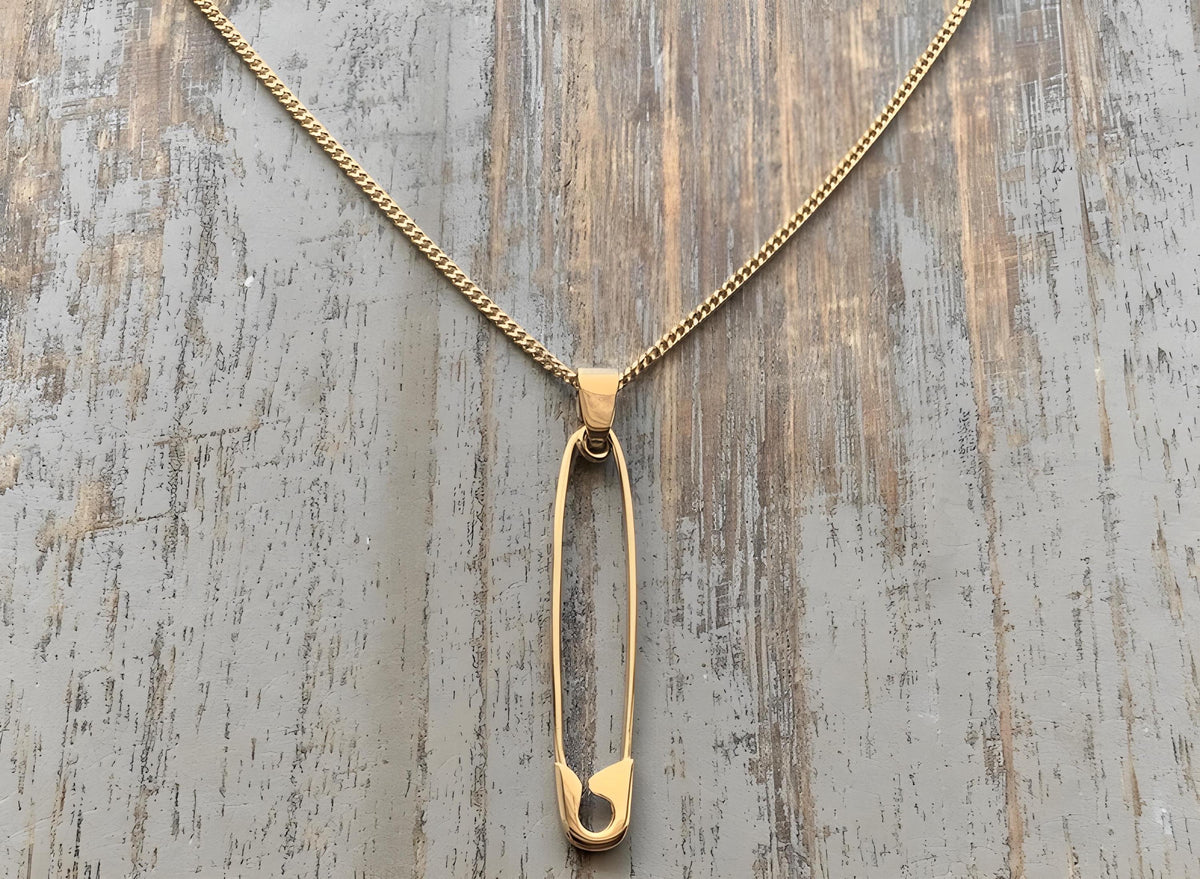 Gold-plated safety pin silver pendant on a delicate gold chain against a rustic wood background.