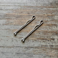 Two sterling silver handmade bobby pins with minimalist loop detail on rustic wooden surface.