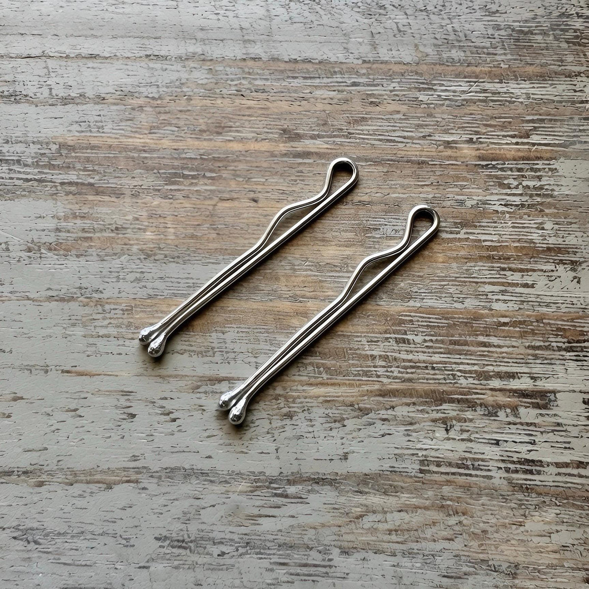 Two sterling silver handmade bobby pins with minimalist loop detail on rustic wooden surface.