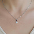 Sterling silver necklace with small evil eye pendant on delicate chain, worn on neck.