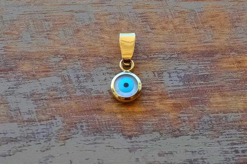Gold plated sterling silver evil eye pendant on wooden background.