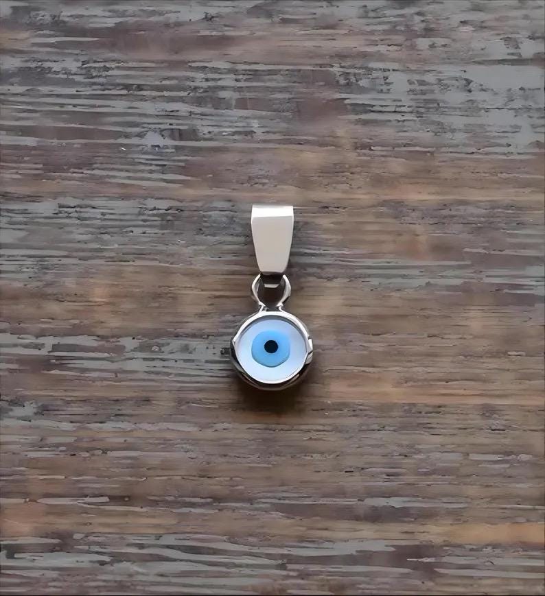 Sterling silver round evil eye pendant with blue, white, and black enamel detailing on wooden background.