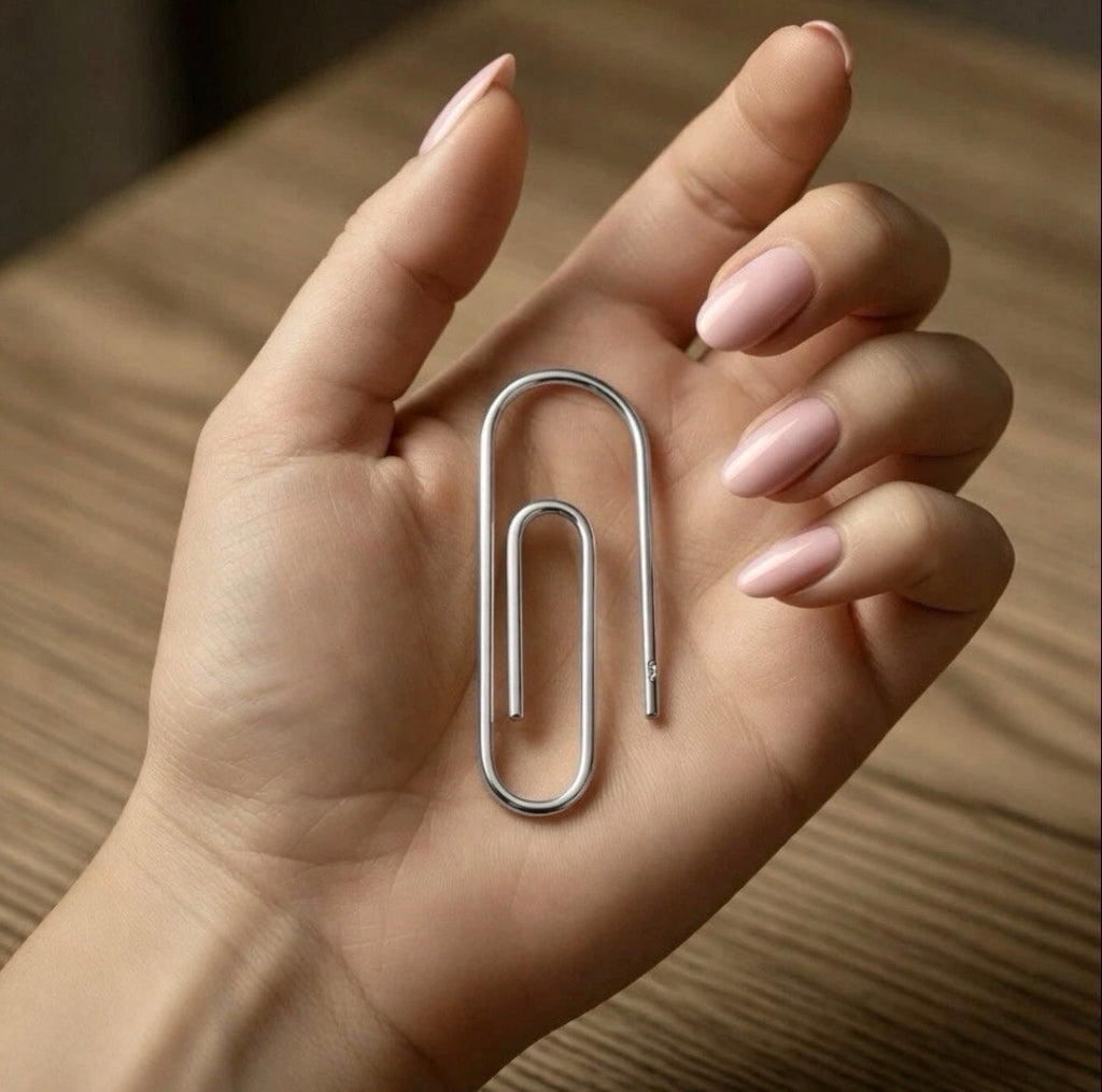 Sterling silver money clip shaped like a large paperclip held in hand with neutral-toned nails.