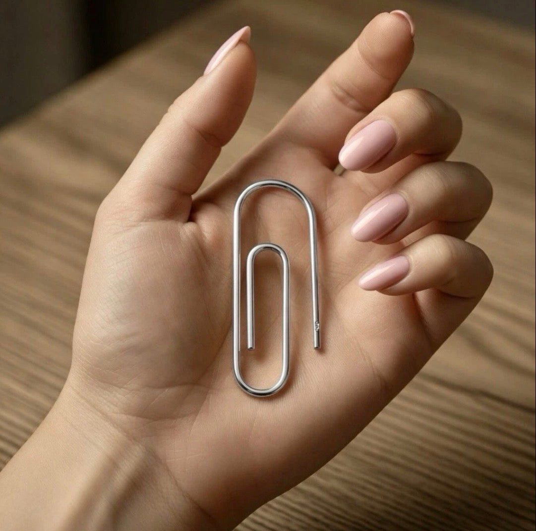 Sterling silver money clip shaped like a large paperclip held in hand with neutral-toned nails.