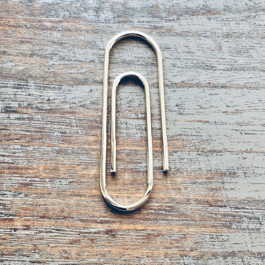 Sterling silver money clip shaped like a large paperclip with smooth polished finish on wood surface.