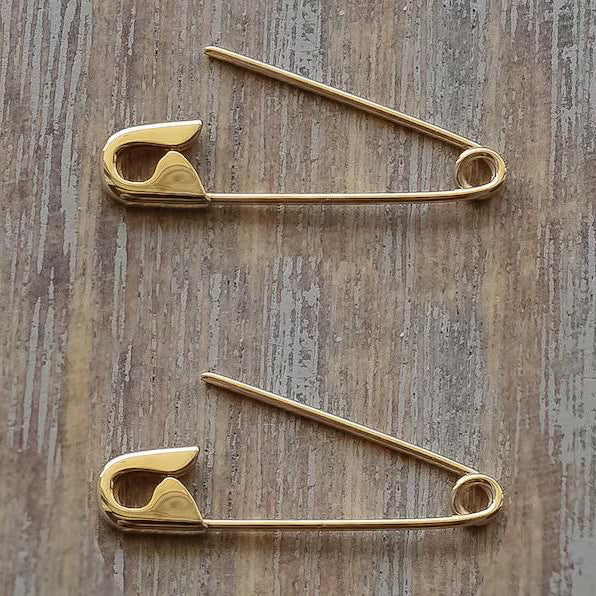 Two gold plated silver safety pin cartilage earrings laid flat on wood surface.