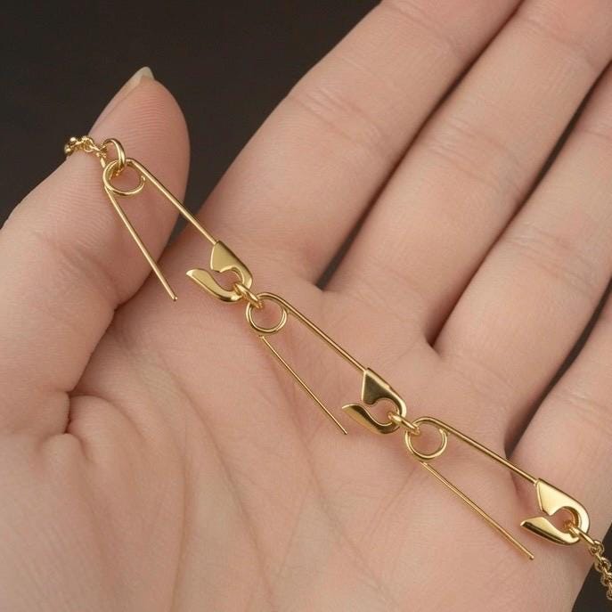 Delicate gold-plated safety pin charm holder necklace in hand of a woman .
