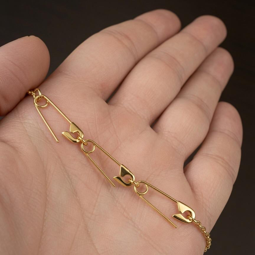 Delicate gold-plated safety pin charm holder necklace in hand.