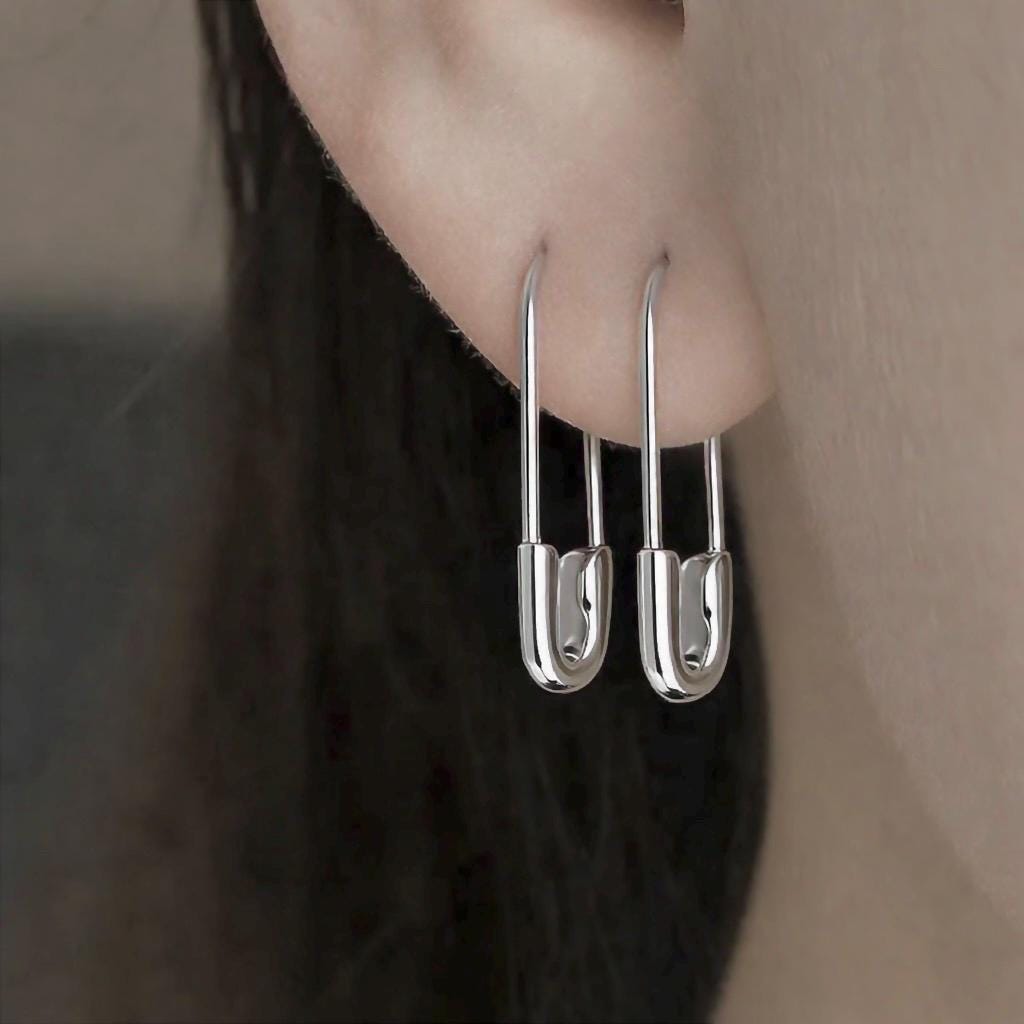 Sterling silver 3/4" safety pin hoop earrings on ear with minimalist punk style.