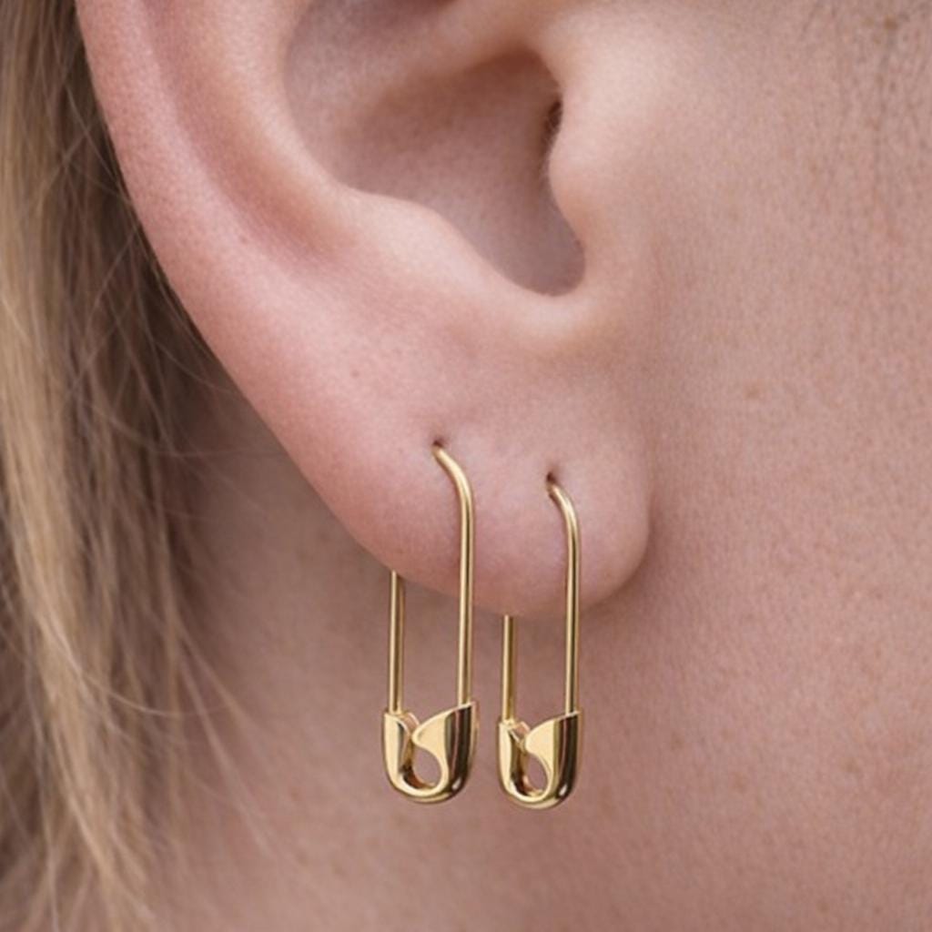 Gold plated 3/4'' hoop silver earrings shaped like safety pins on ear.