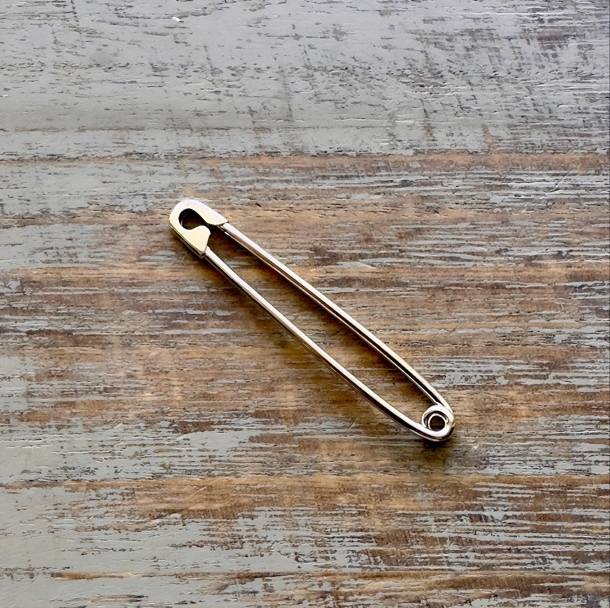 Sterling silver industrial safety pin earring with 1.75-inch length and 16 gauge thickness on wood surface.