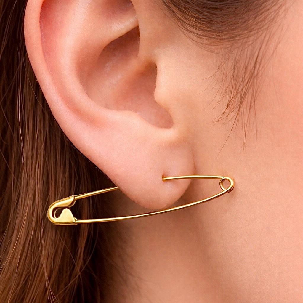 Gold plated long safety pin earring worn on earlobe with sleek wire design.