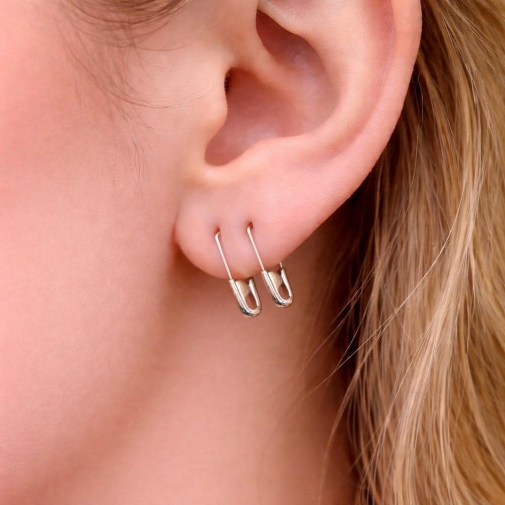 Sterling silver mini safety pin earrings worn on earlobe with smooth, shiny finish.