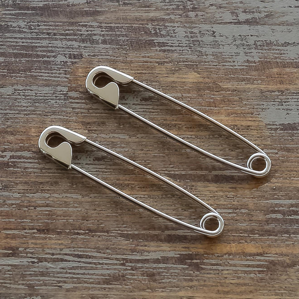 Pair of 1.25-inch sterling silver safety pin earrings with a minimalist, polished finish on wooden surface.