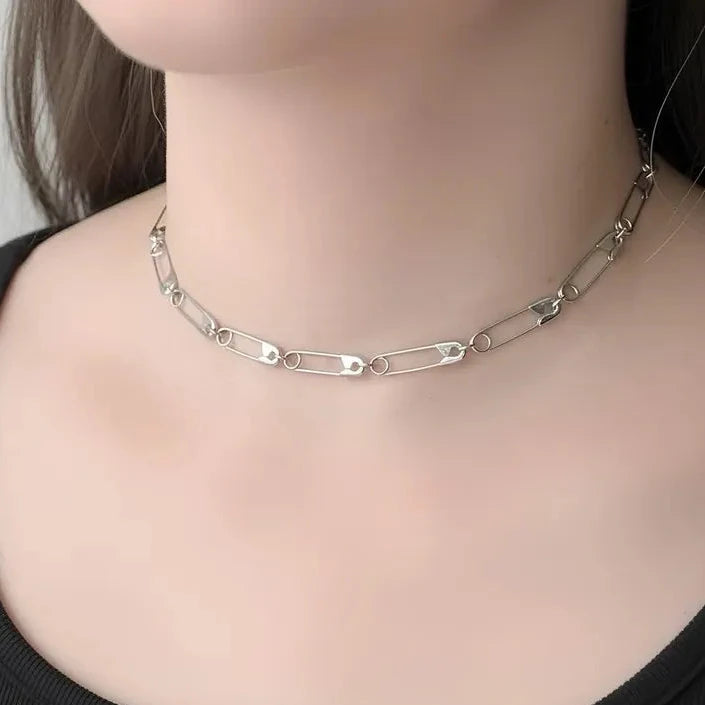 Sterling silver choker necklace made of linked safety pin charms on model's neck.