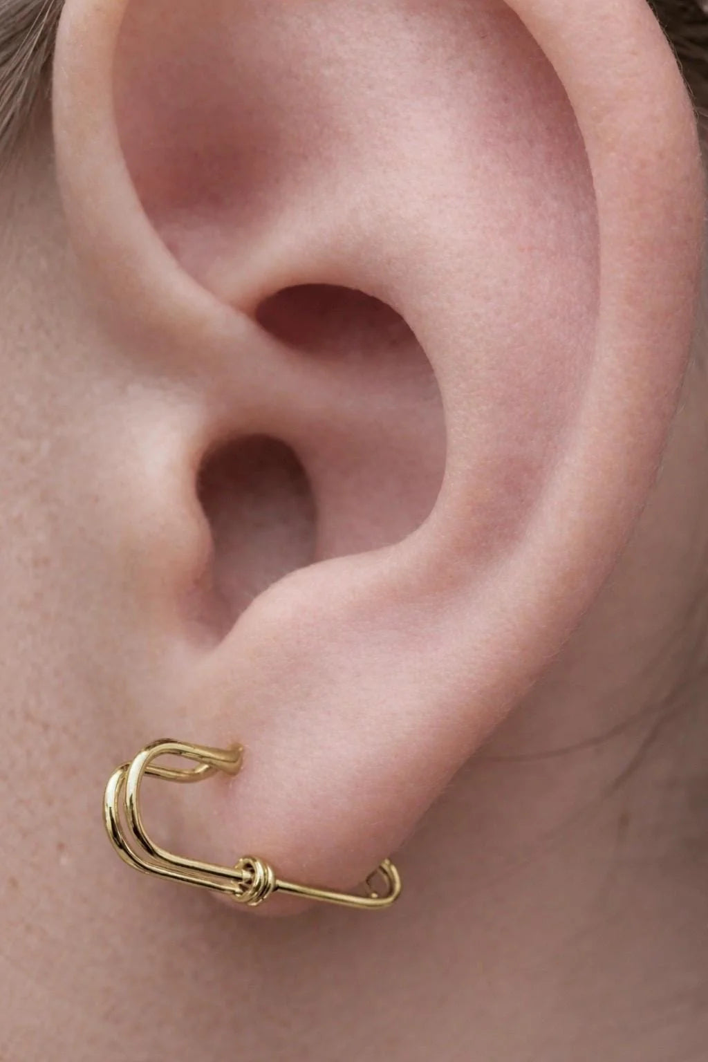 Gold plated silver small safety pin wire earring on ear with minimalist edgy design.