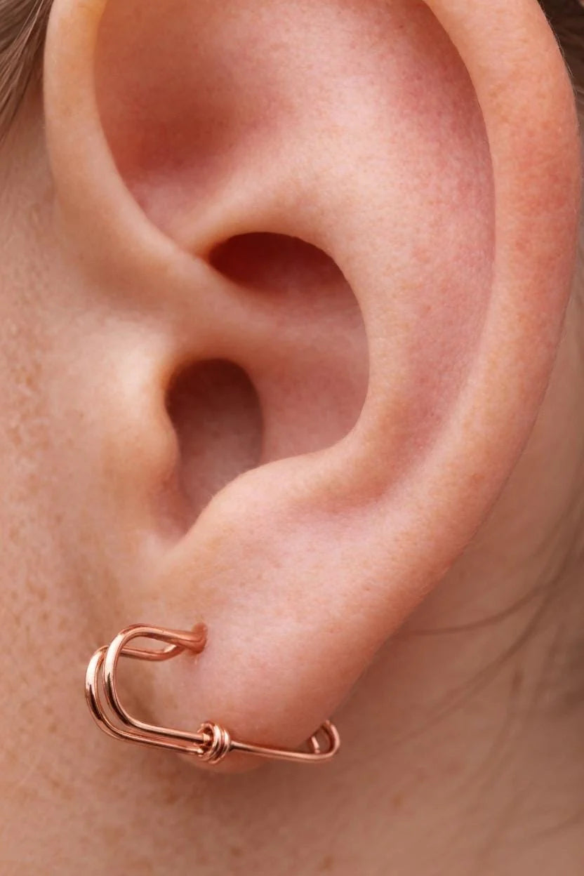 Small rose gold plated silver safety pin shaped earring worn on earlobe with a minimalist, industrial design.