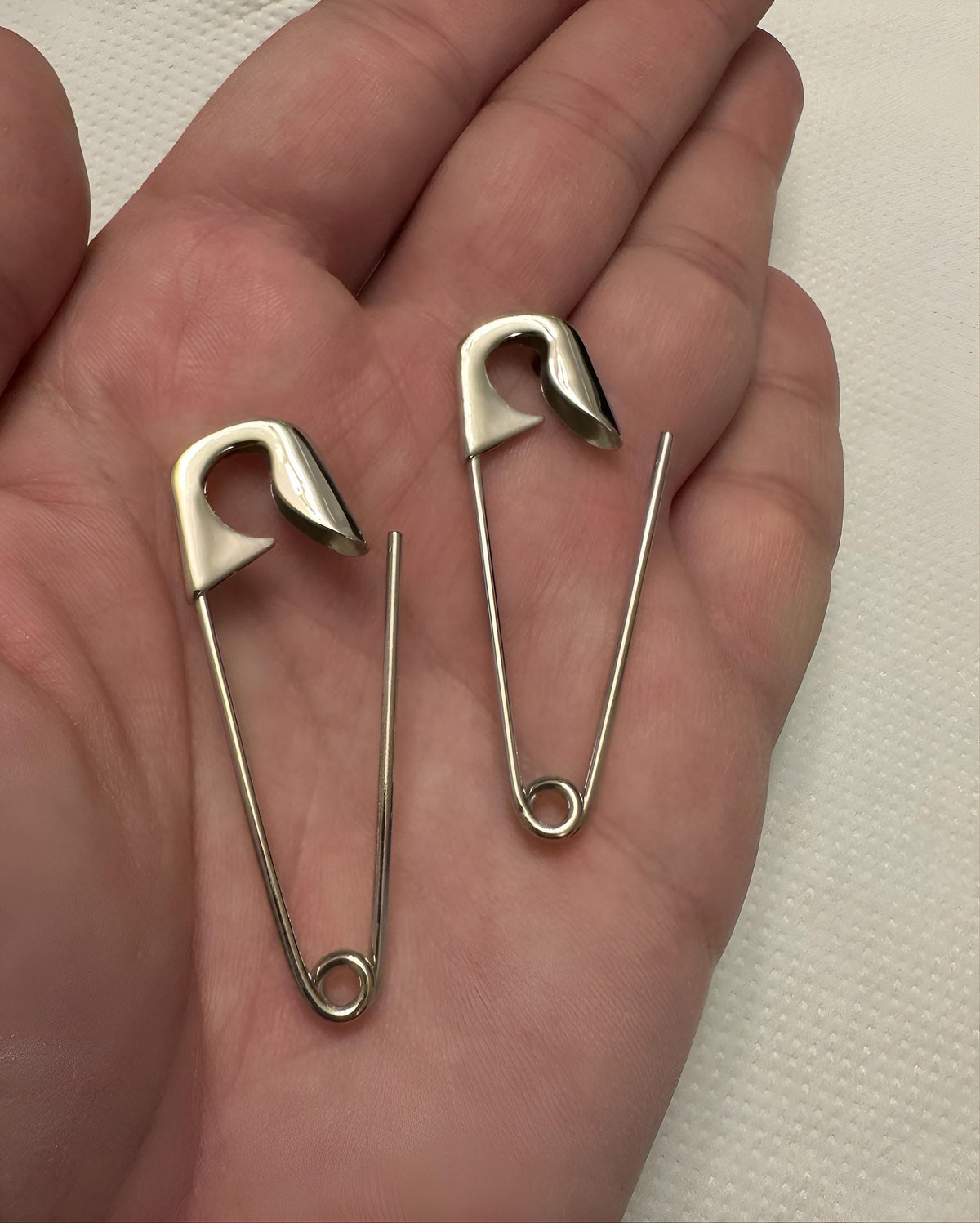 Large sterling silver safety pin earrings 2 inches with shiny finish, shown resting on hand.