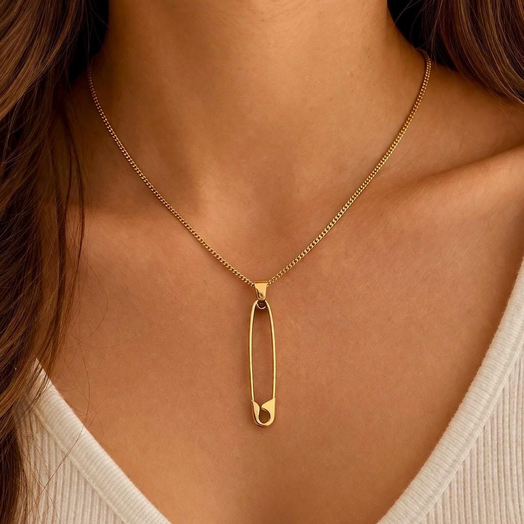 Gold plated safety pin pendant necklace with delicate chain on model's neck.
