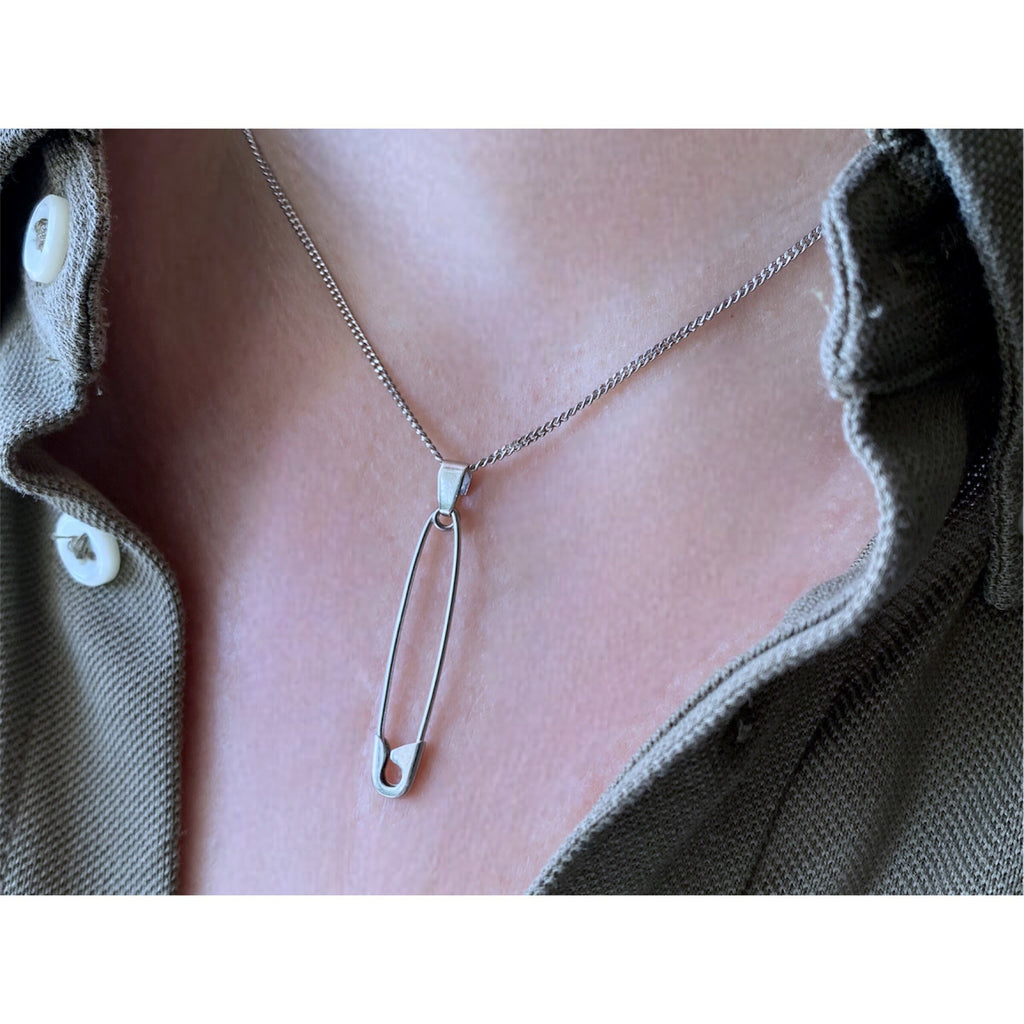 Sterling silver safety pin pendant necklace on delicate chain, worn with olive green shirt collar.