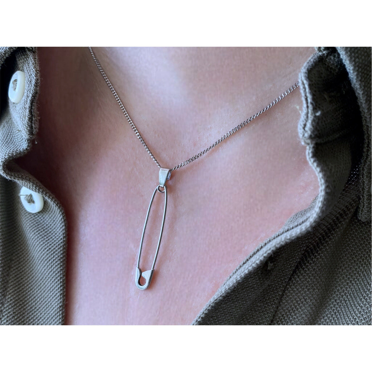 Sterling silver safety pin pendant necklace on delicate chain, worn with olive green shirt collar.