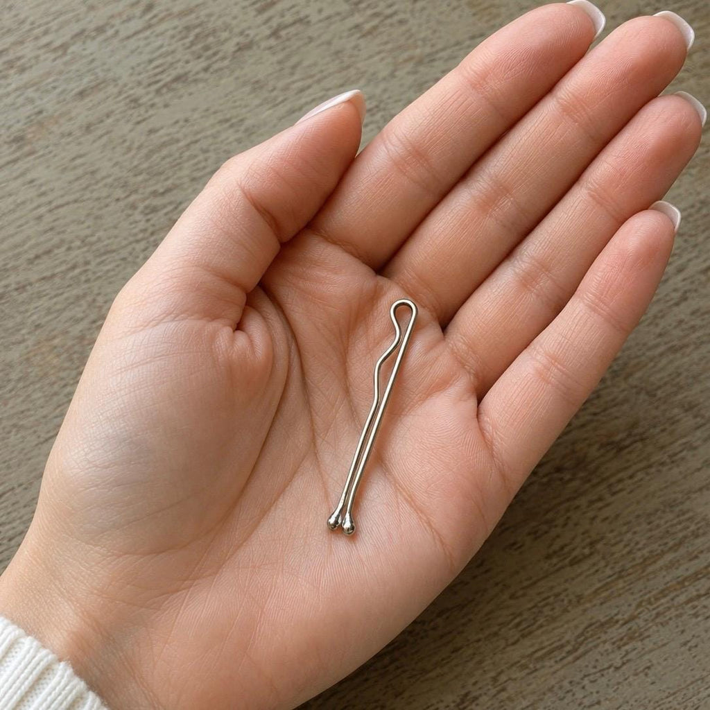 Shiny solid white gold bobby pin with a minimalist, smooth curved design held in a hand.