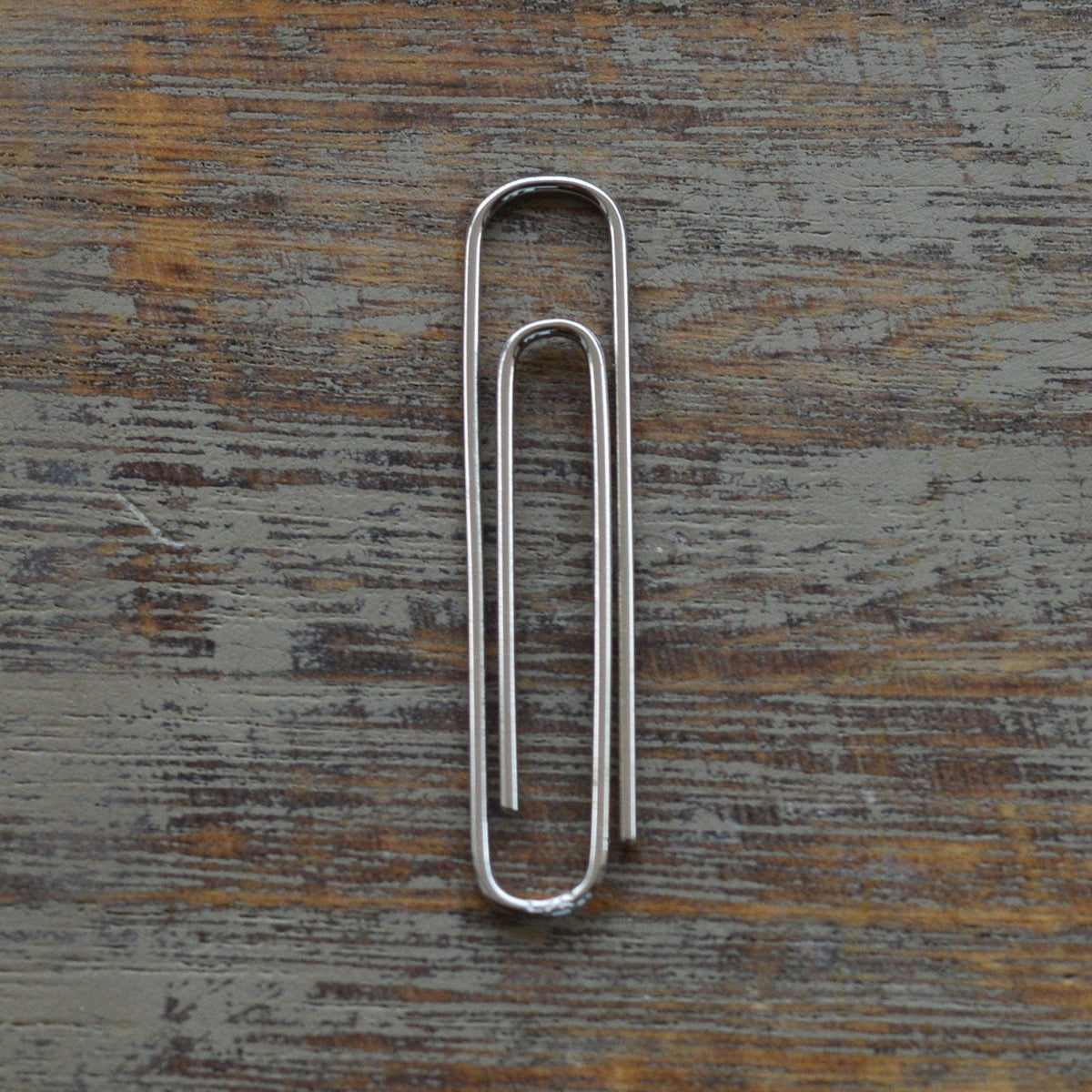 Slim white gold metal money clip with smooth rounded edges on rustic wooden background.