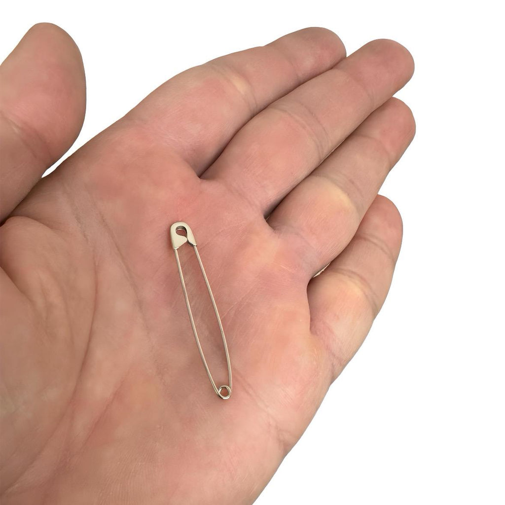 Delicate white gold long safety pin earring with smooth polished finish, 1.75 inches long, held on open palm.