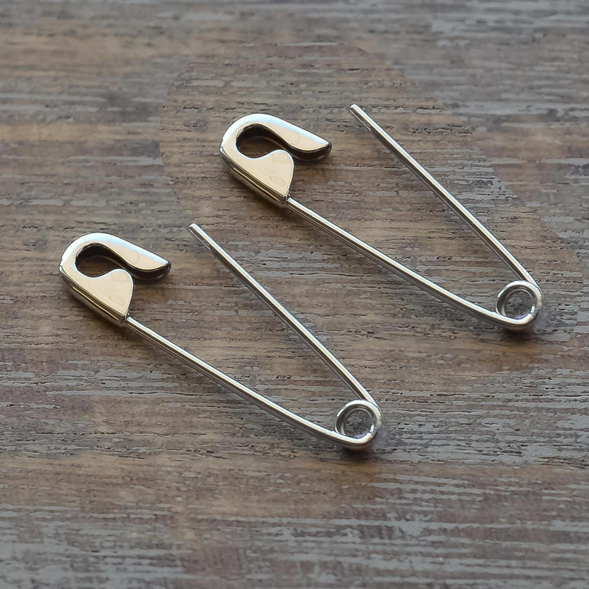 Pair of 1-inch gold safety pin cartilage earrings with a shiny finish on wood surface.