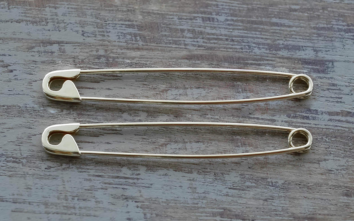 Pair of long  white gold safety pin earrings measuring 1.75 inches on wooden surface with a sleek, minimalist design.