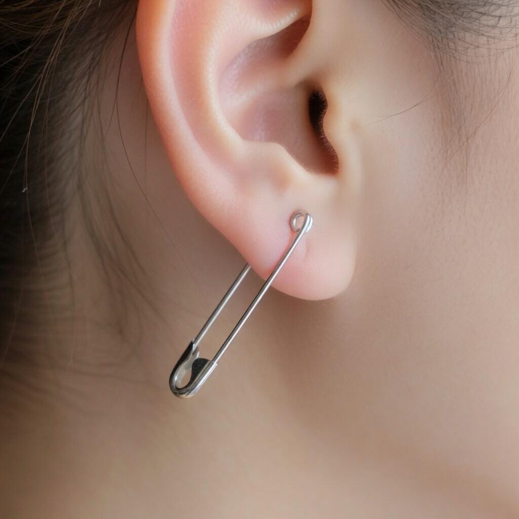 Single slender white gold safety pin earring worn on the earlobe, minimalist punk style.