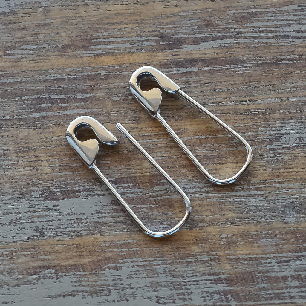 White Gold-tone safety pin shaped hoop earrings with minimalist, edgy design on wood surface.