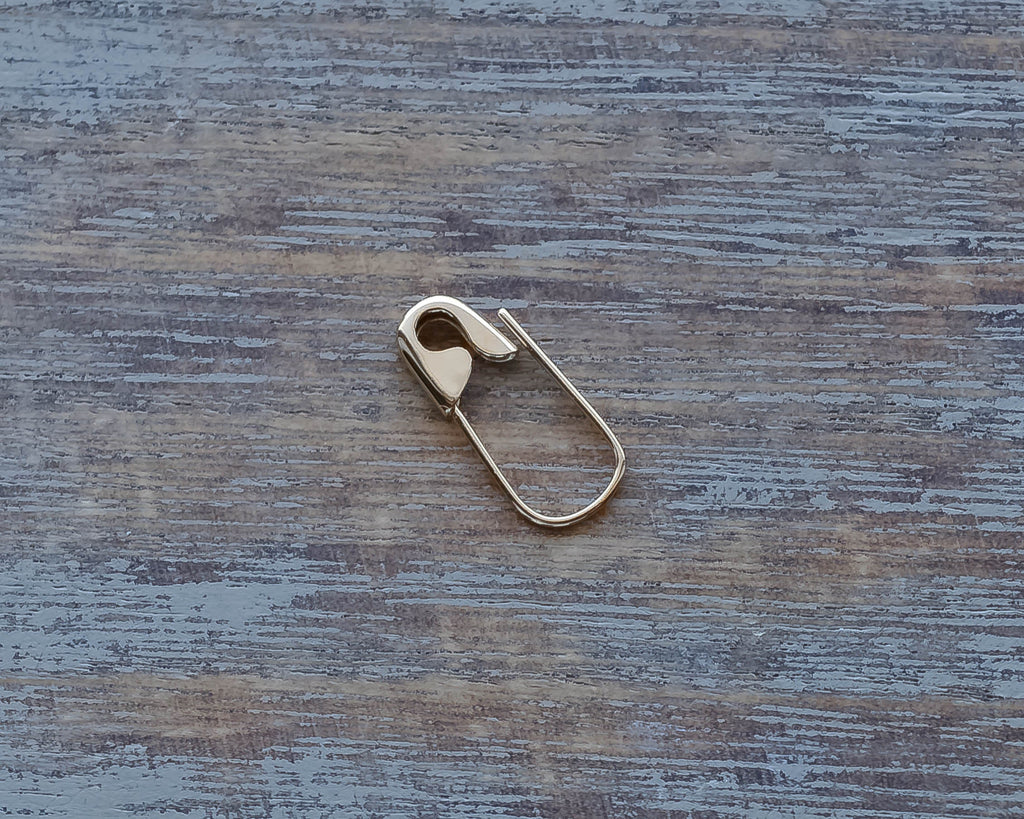 White Gold mini safety pin earring with a sleek, smooth finish on wood background.