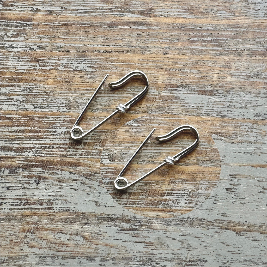 Pair of small white gold safety pin wire earrings on rustic wooden surface