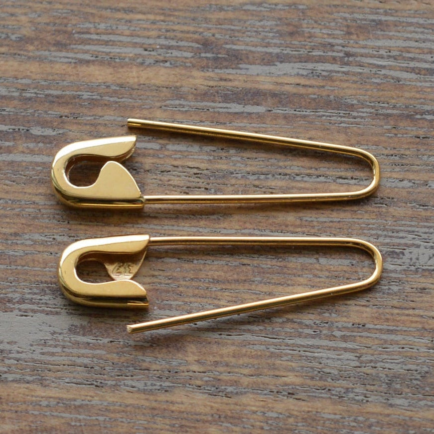 Pair of gold safety pin hoop earrings, 1 inch, polished finish on wooden surface.