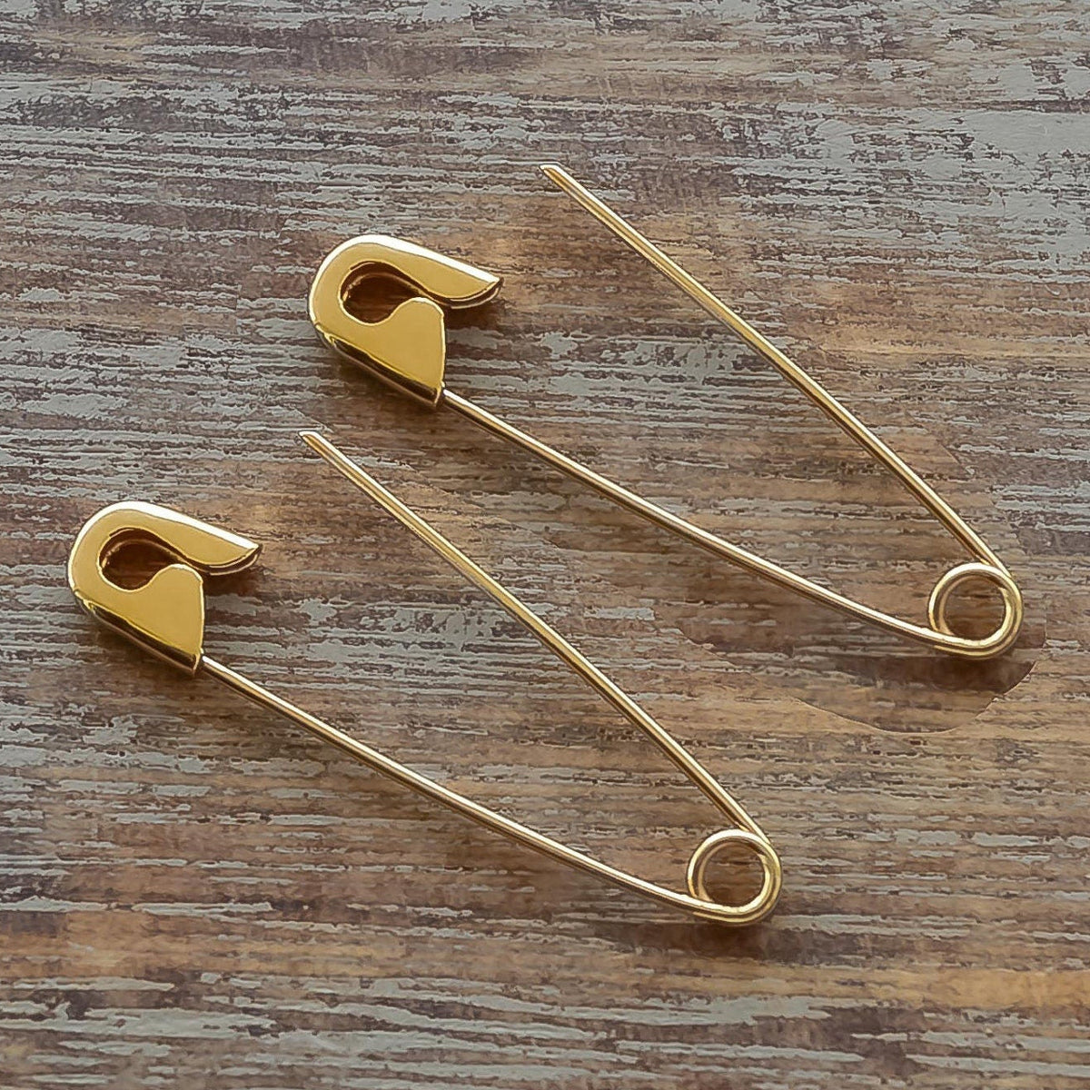 Pair of gold safety pin earrings with a polished finish on a wooden surface.