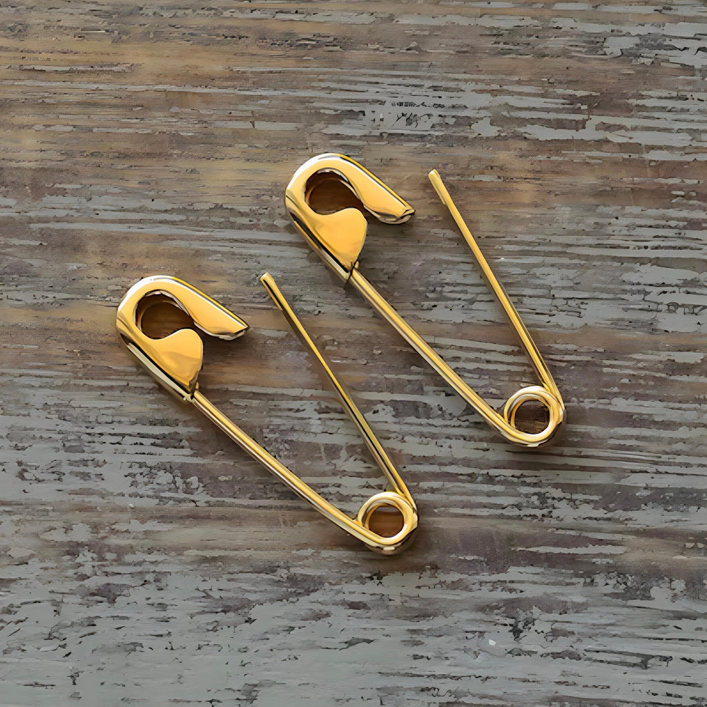 Pair of shiny gold safety pin earrings measuring 3/4 inch with smooth finish and modern design on wooden surface .