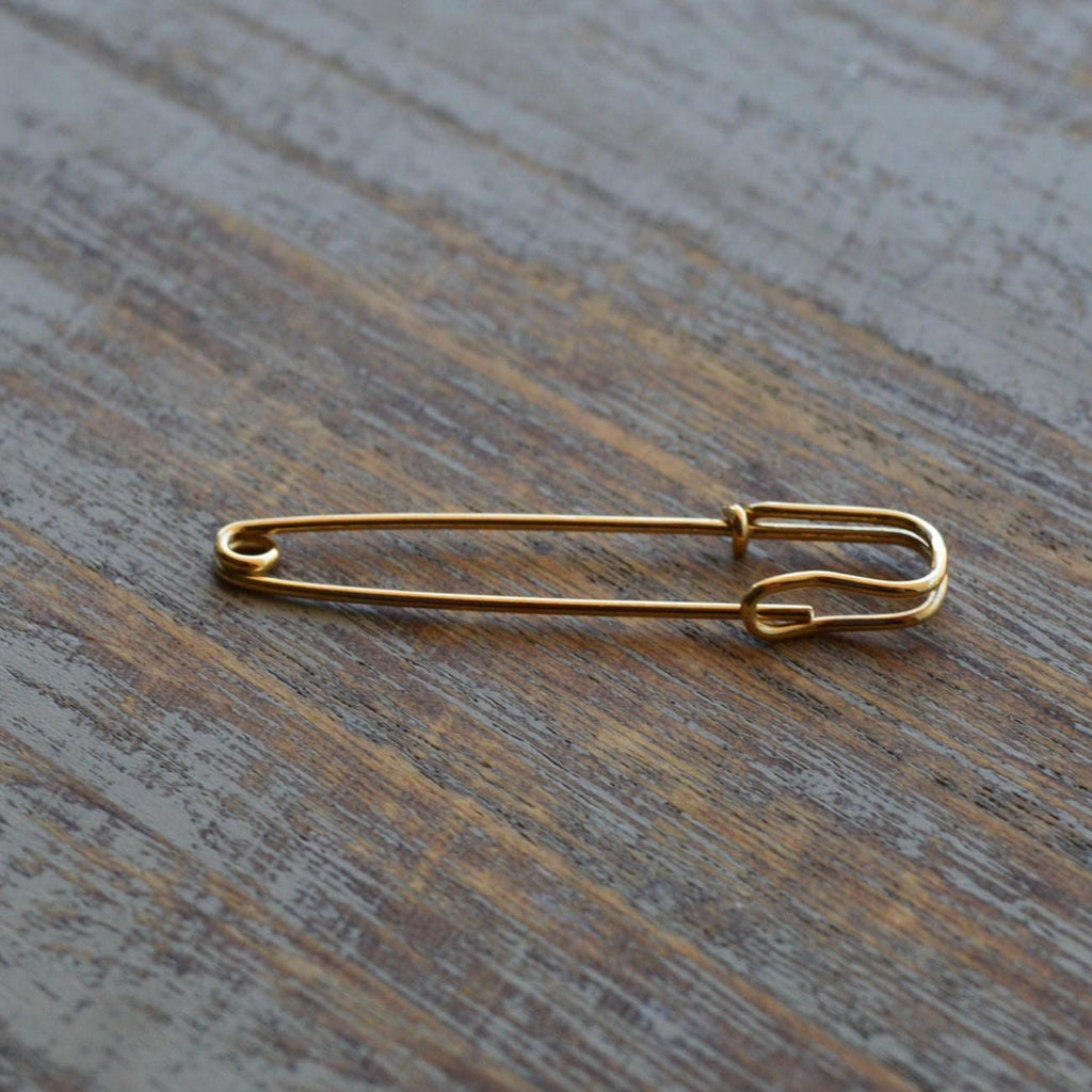 Delicate 1.25-inch yellow gold wire safety pin earring on wooden surface.