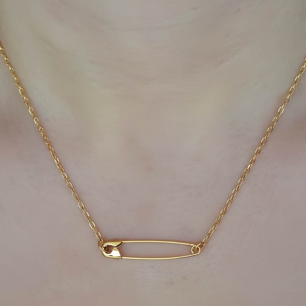 Gold plated minimalist safety pin necklace with delicate chain on neckline.
