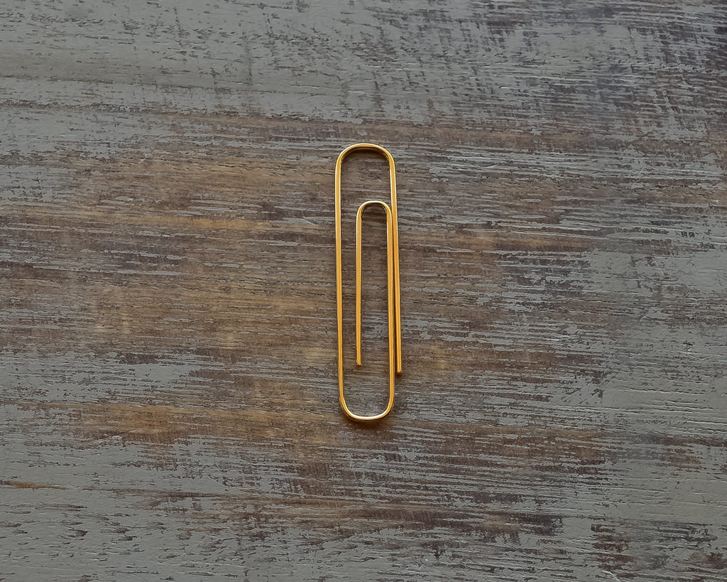 Gold plated shiny paperclip money clip on rustic wooden surface.