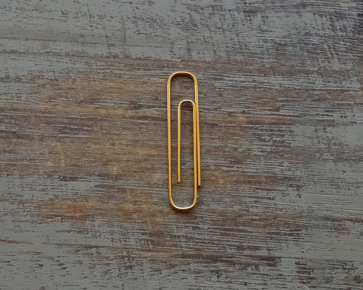 Gold plated shiny paperclip money clip on rustic wooden surface.