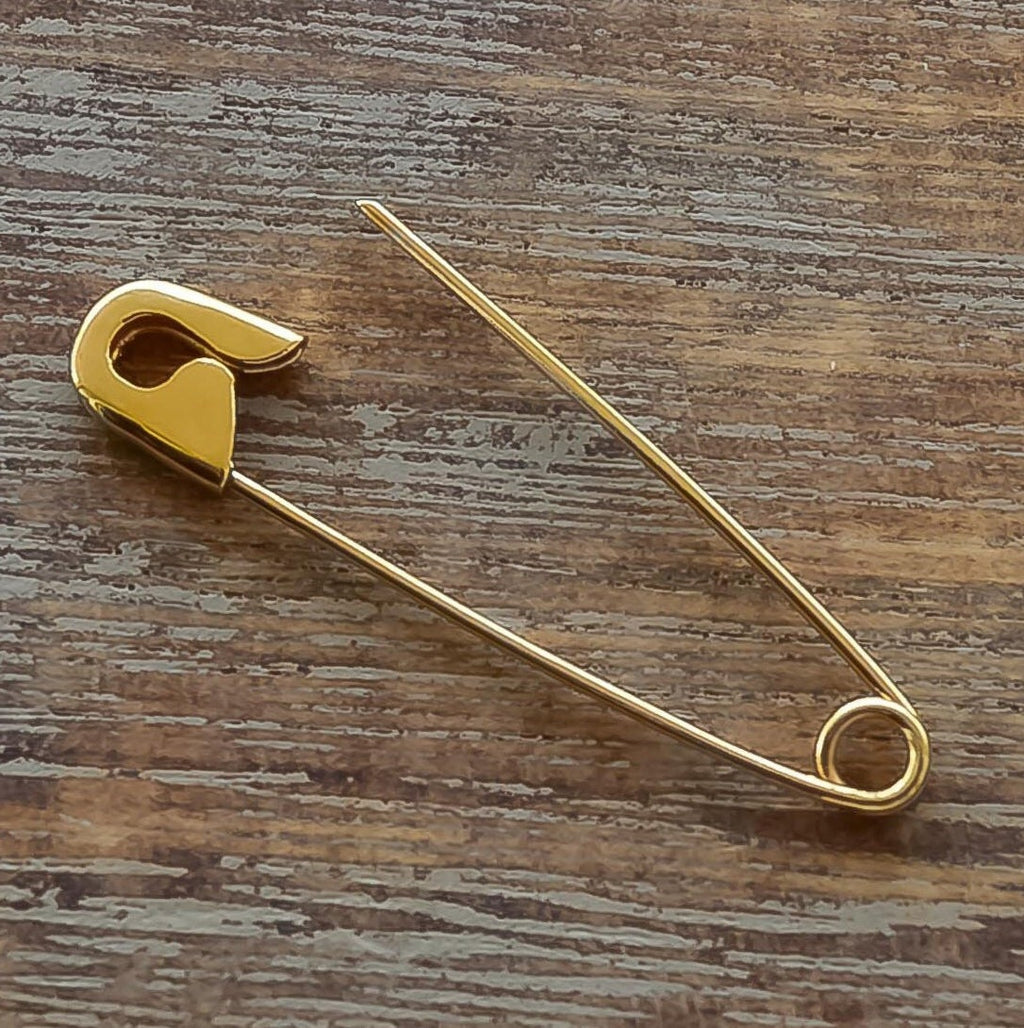 Minimalist gold safety pin earring with polished finish on wooden surface background.