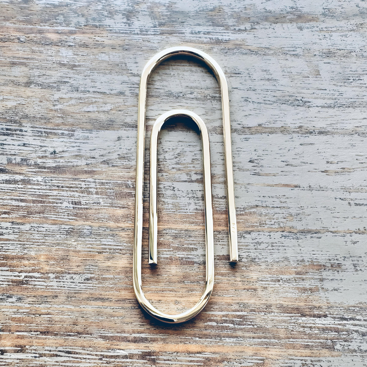 Handcrafted gold paperclip-style money clip with a smooth, minimalist design on rustic wood background.