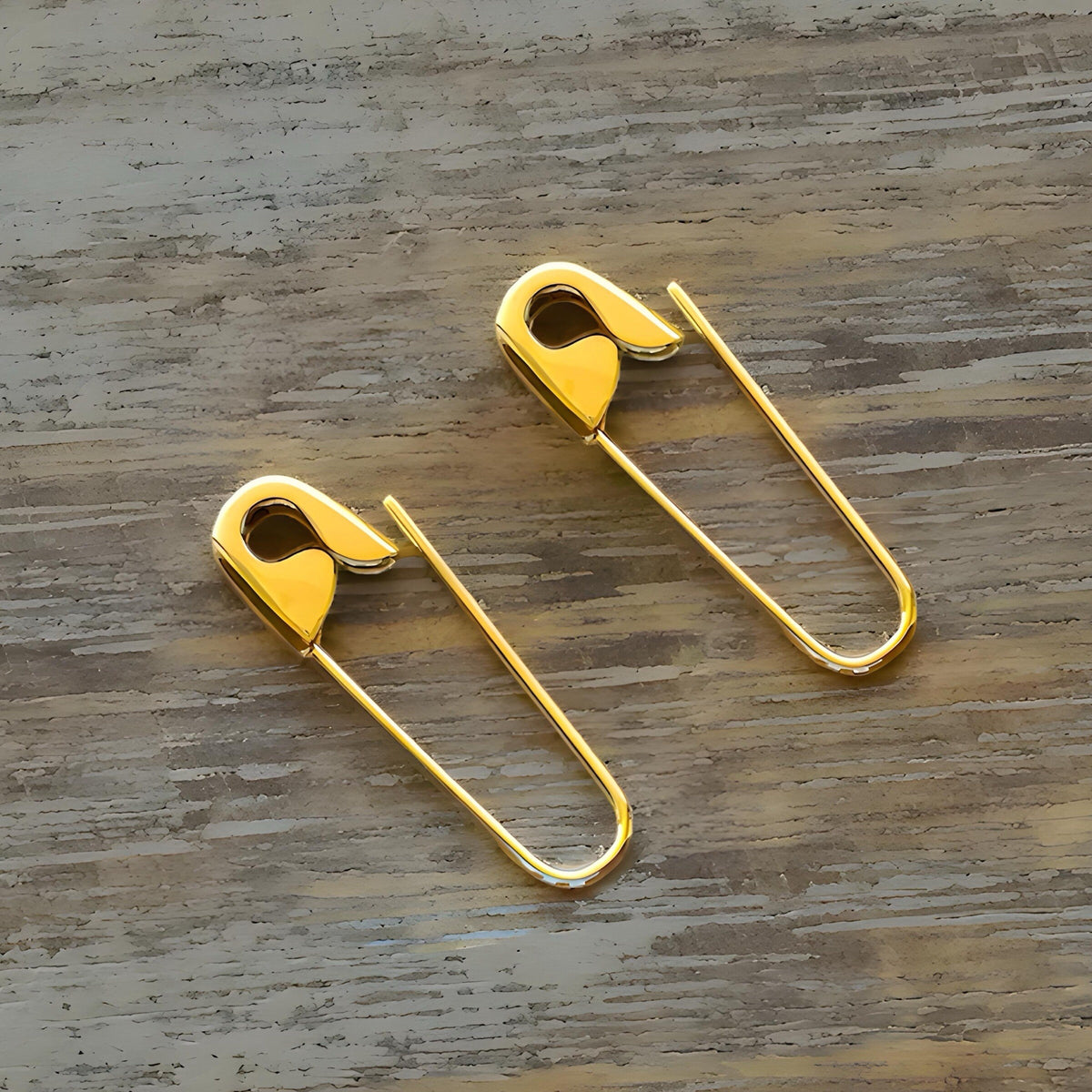 Pair of polished gold-tone safety pin hoop earrings measuring 3/4 inch with minimalist, edgy design.