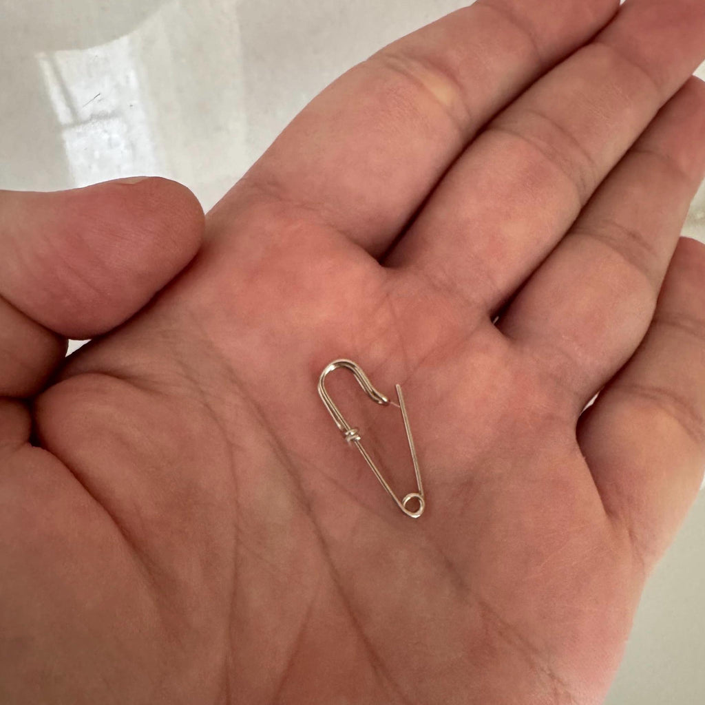 Small sterling silver safety pin earring with a sleek, minimal wire design held in palm.