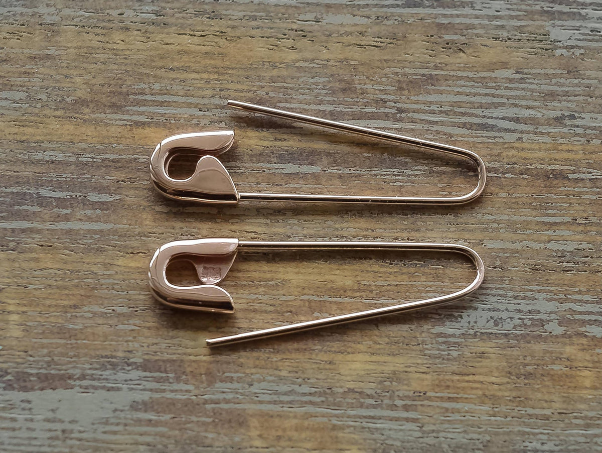 Pair of rose gold plated safety pin hoop earrings on wooden surface.